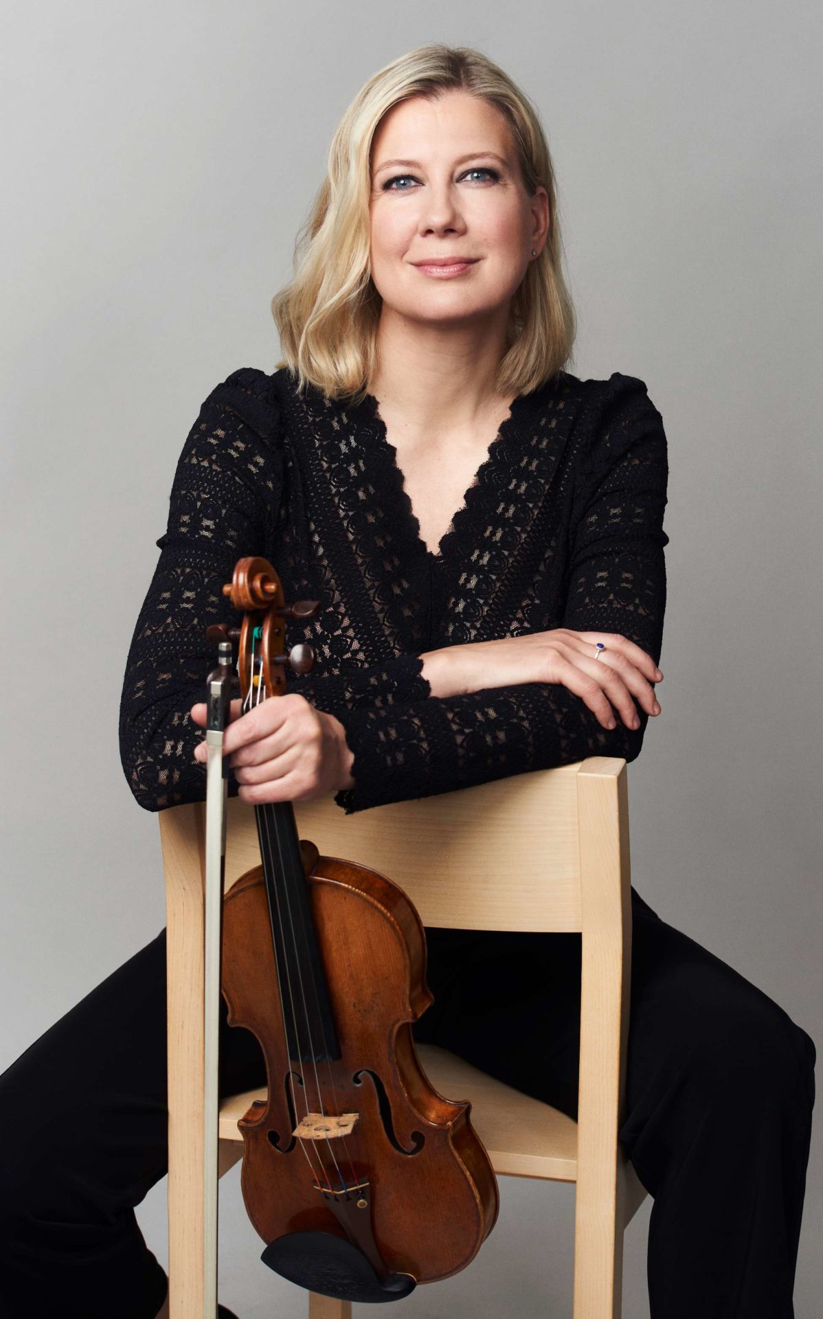 Naantalin Musiikkijuhlien taiteellinen johtaja viulisti Elina Vähälä istuu tuolilla ja pitää viulua kädessään.
